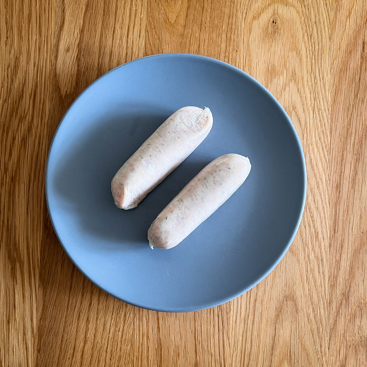 Two raw sausages on a grey plate.