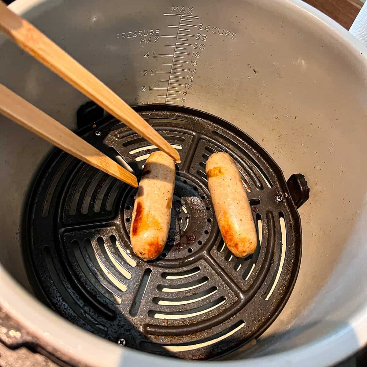 Two sausages in an air fryer partially cooked.