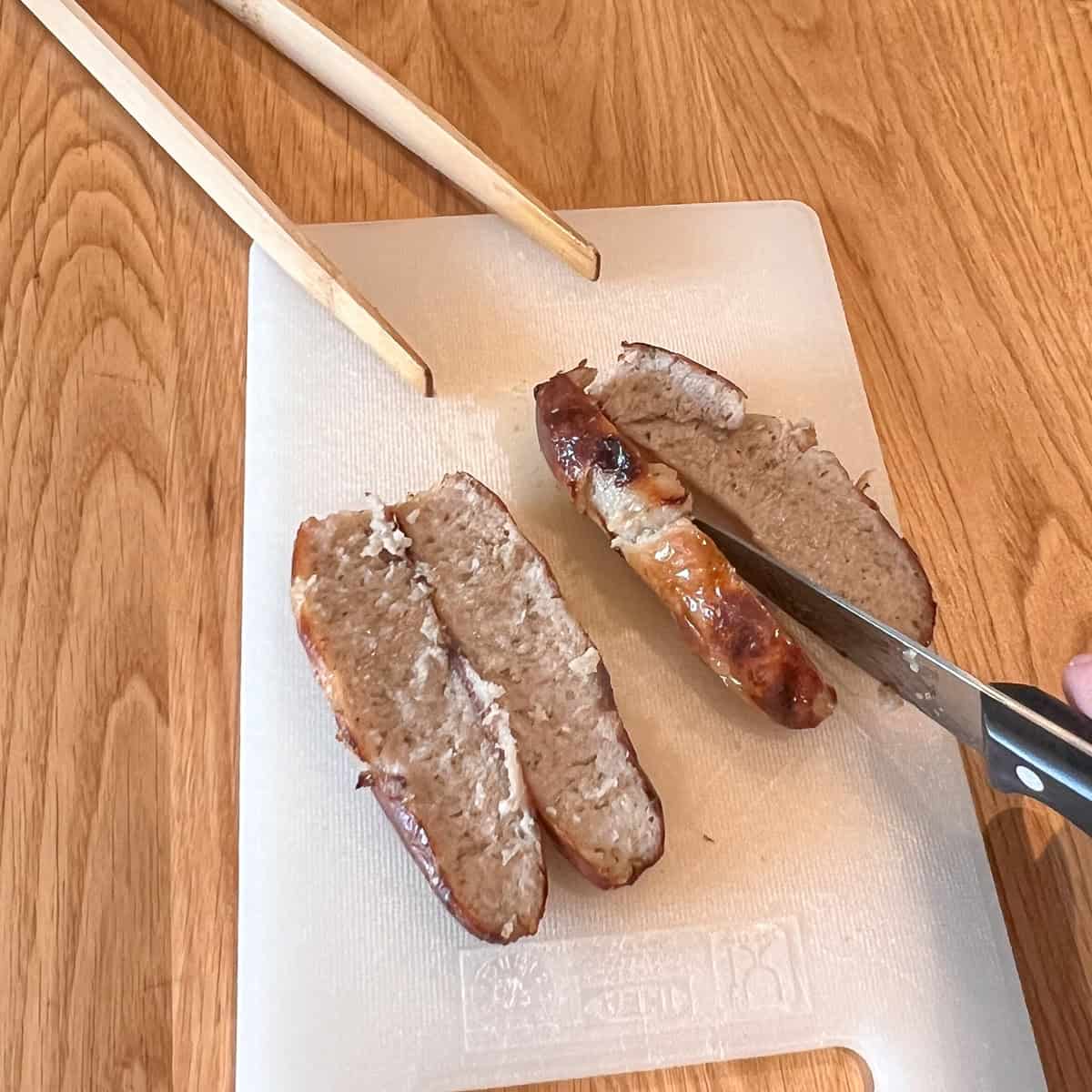 Two cooked sausages sliced lengthways on a chopping board.