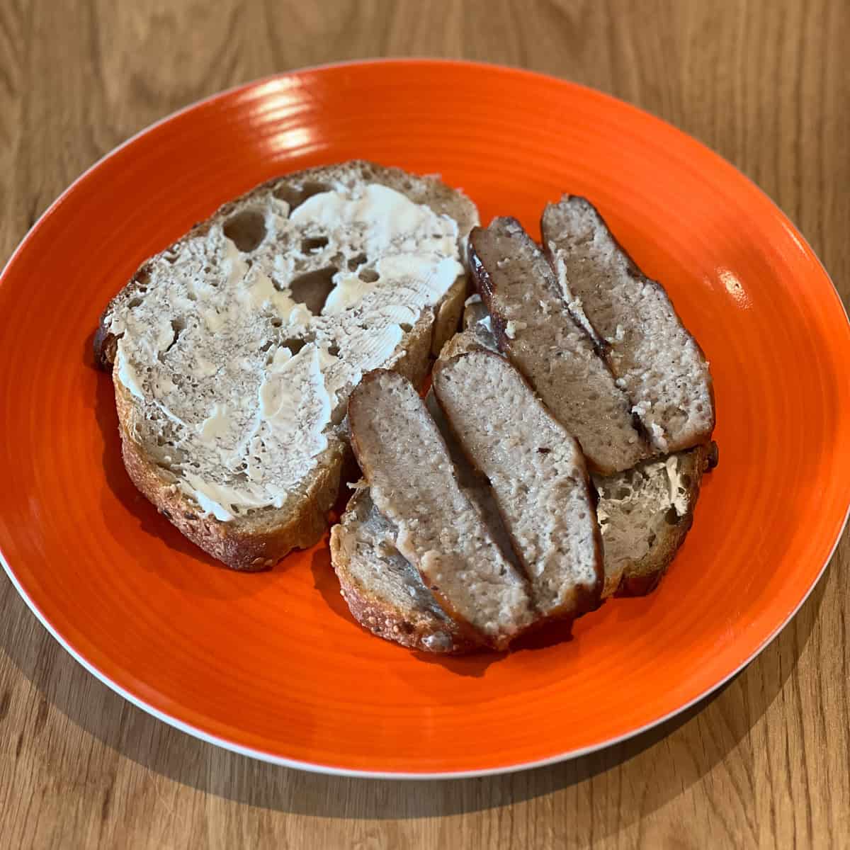 Two sausages sliced on a piece of buttered bread.