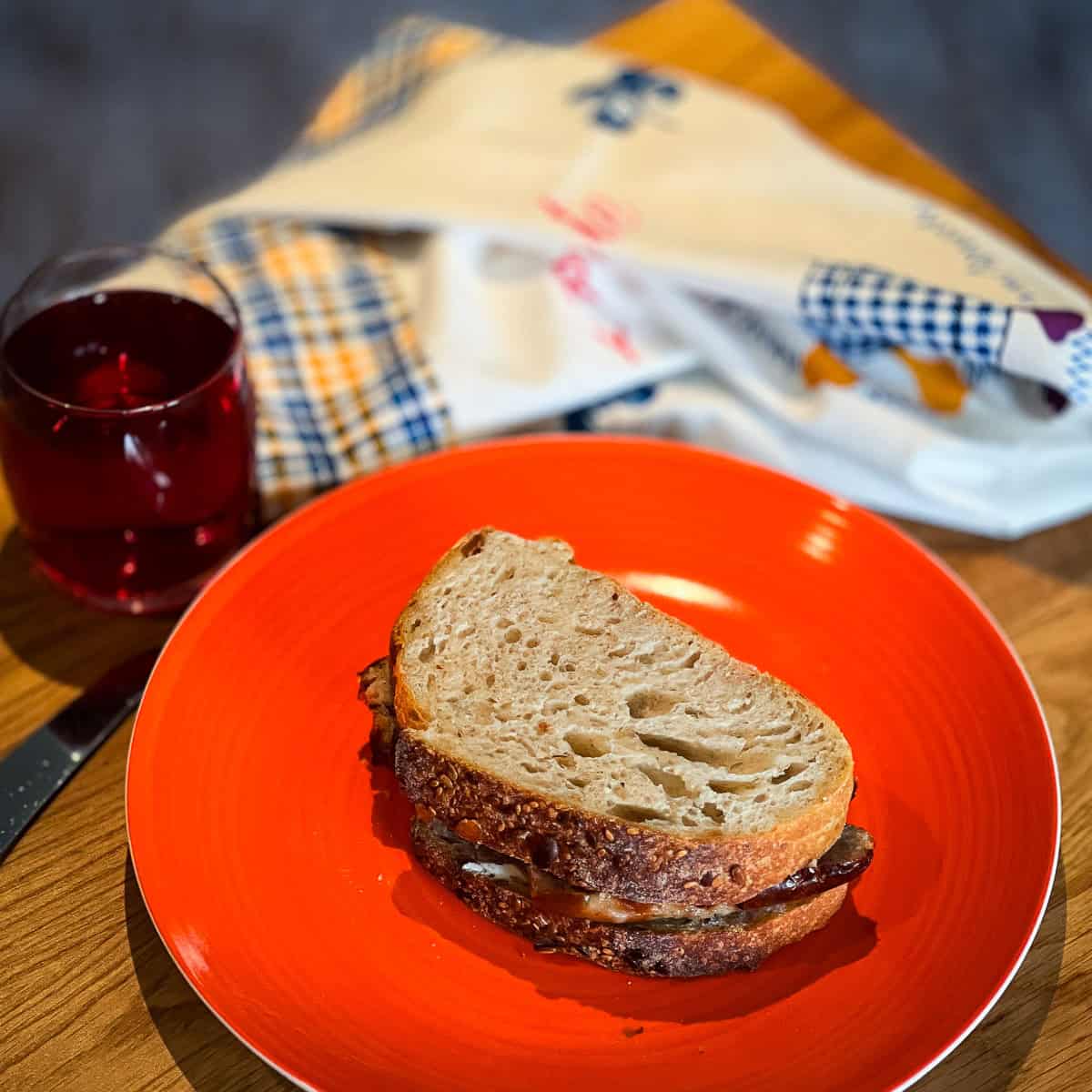 A sausage sandwich on a plate next to a glass of cranberry juice.