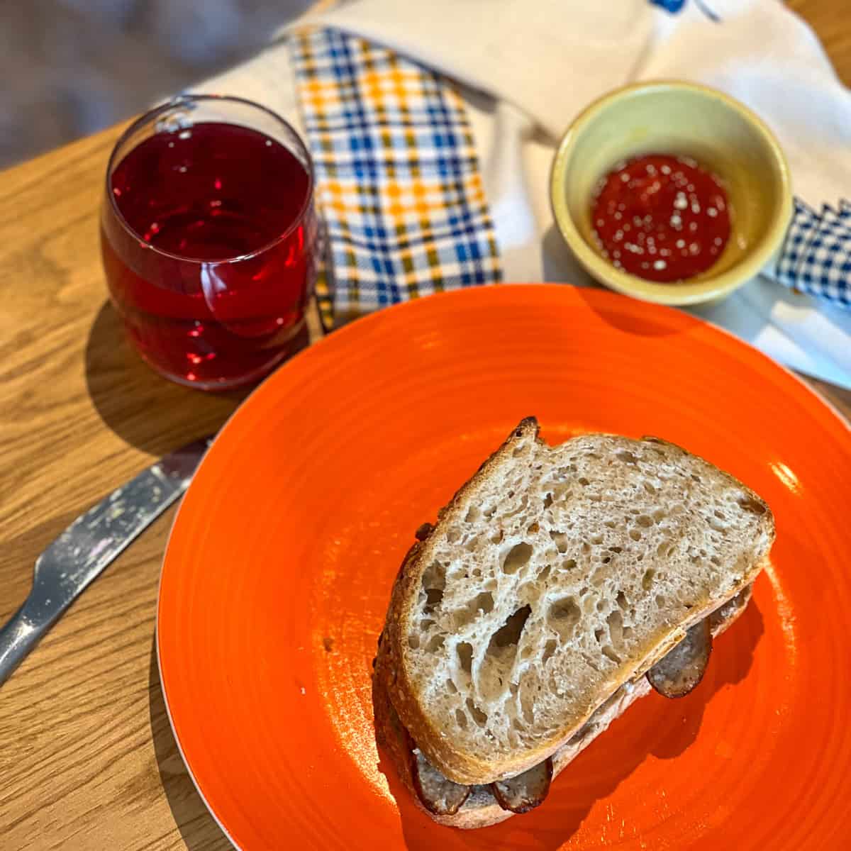 A sausage sandwich on an orange place next to some ketchup.