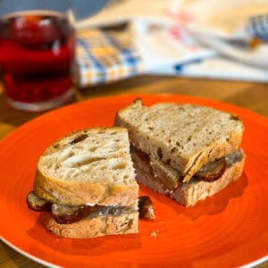 A sausage sandwich sliced in half on an orange plate.