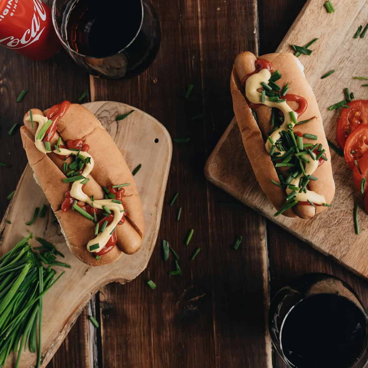 Two hot dogs with mayo on wooden serving boards.