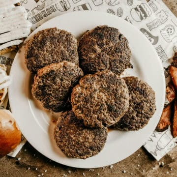 Six cooked burger patties on a white plate.