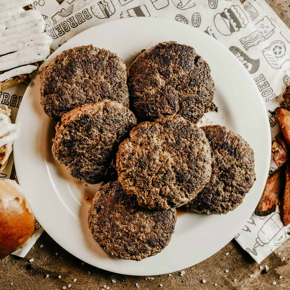 Six cooked burger patties on a white plate.