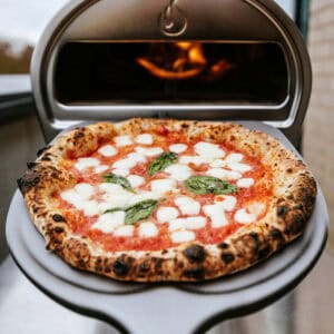A margarita pizza on a peel coming out of a pizza oven.
