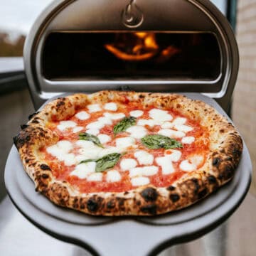 A margarita pizza on a peel coming out of a pizza oven.