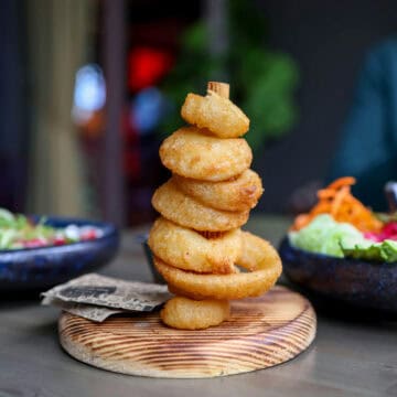 A stack of crispy beer battered onion rings on a wooden spike.