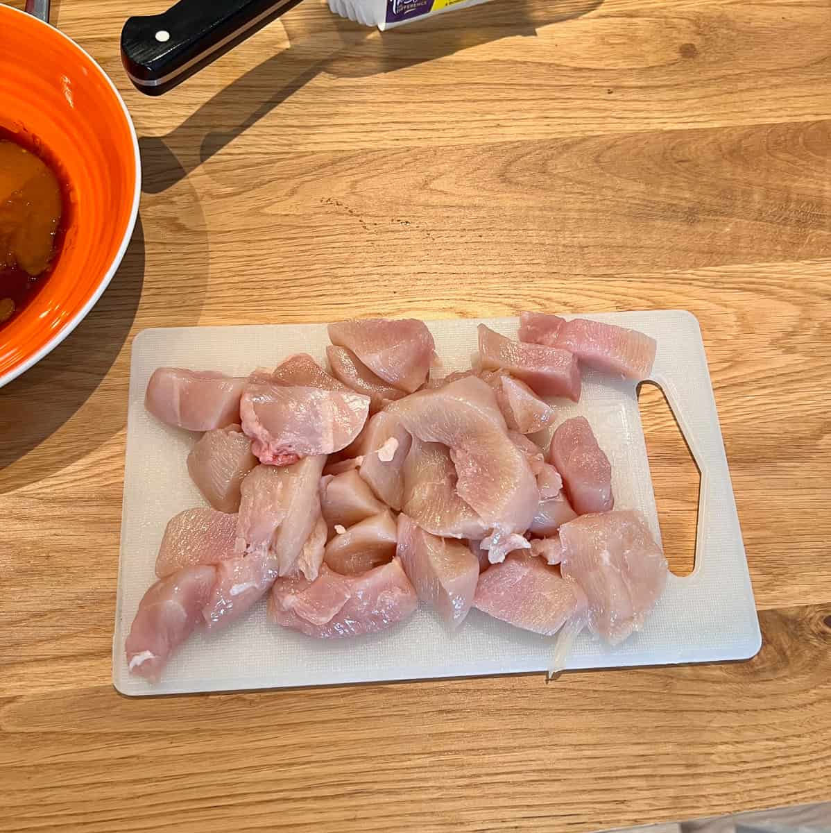 Raw chicken diced on a chopping board.