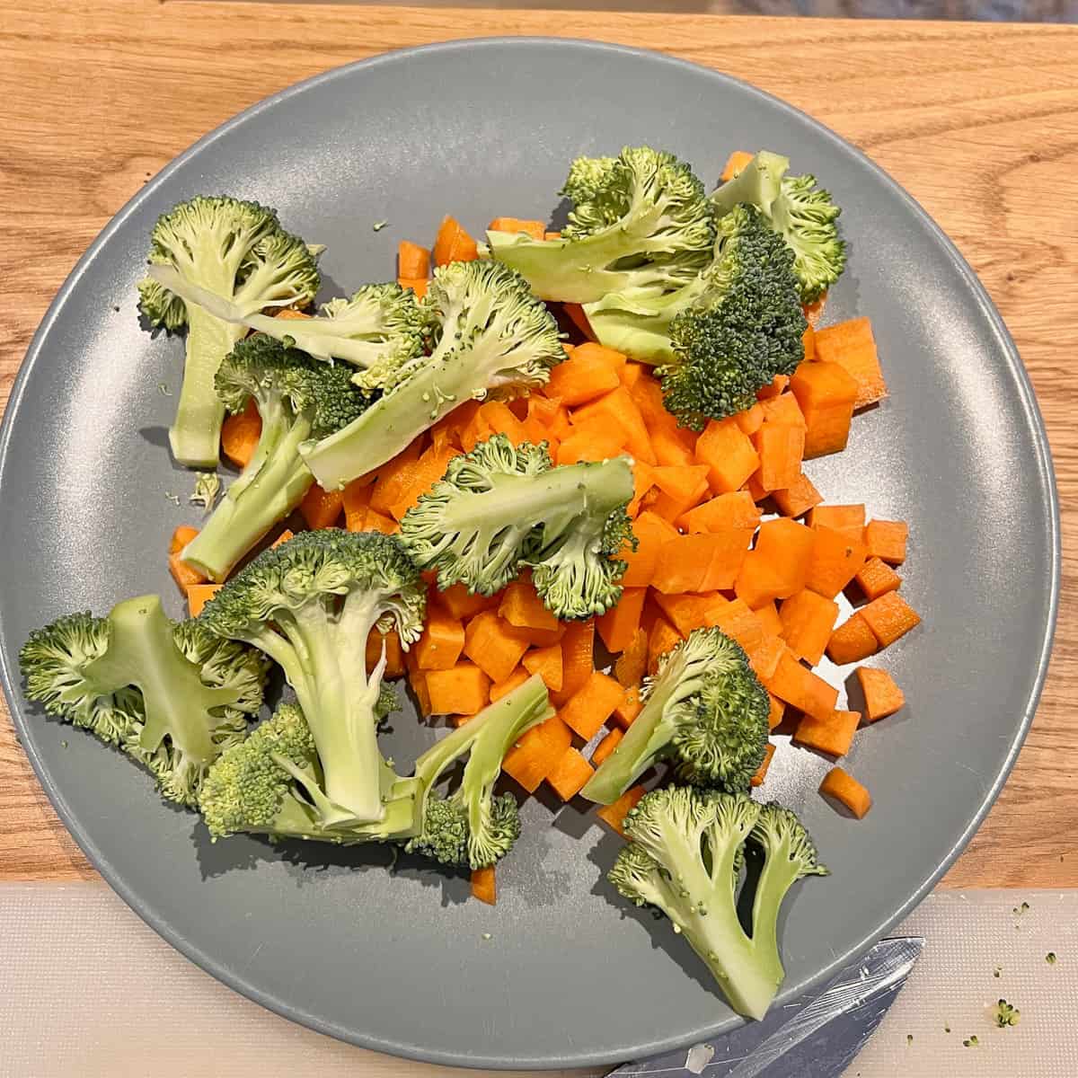 Chopped up broccoli and carrots on a grey plate.
