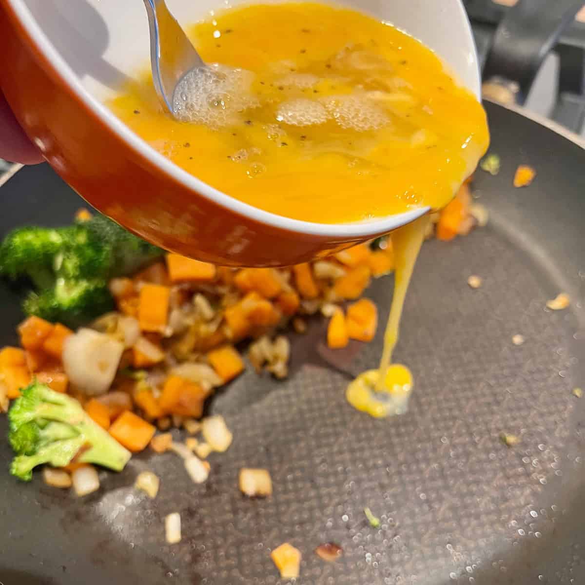 Mixed raw eggs being poured into a frying pan.