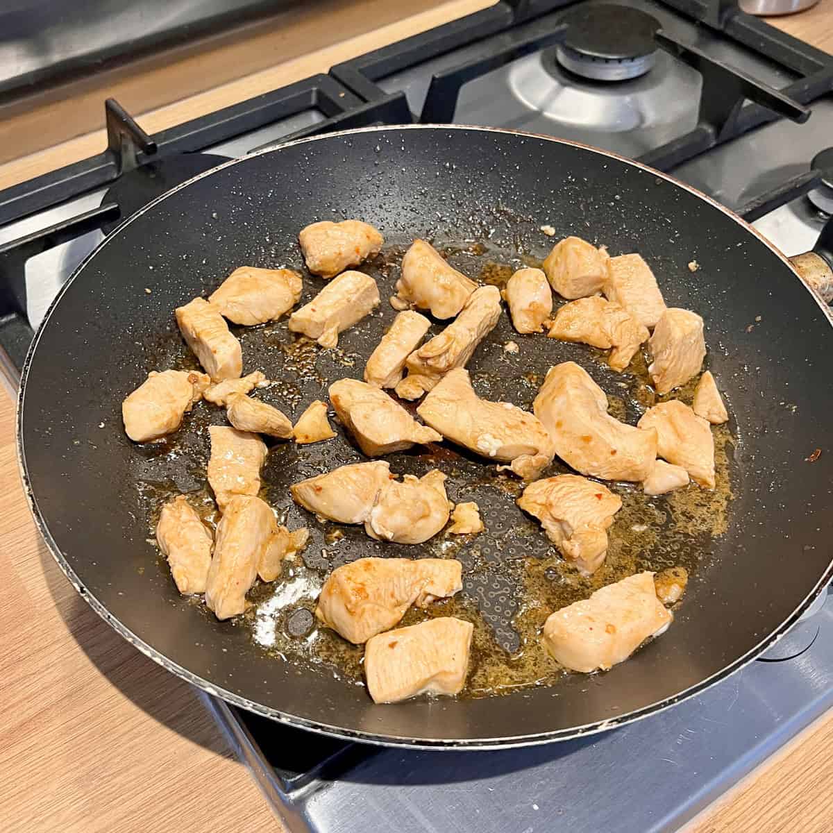 Chicken pieces cooking in a frying pan.