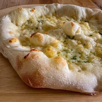 Garlic pizza bread on chopping board.