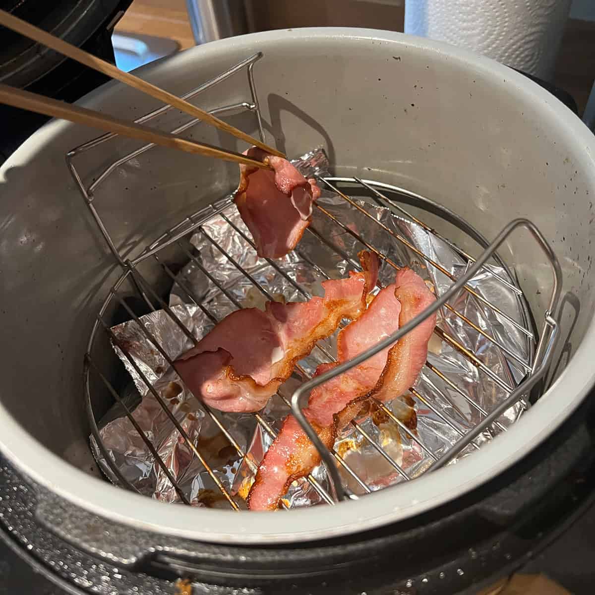 Turning bacon with tongs in an air fryer.