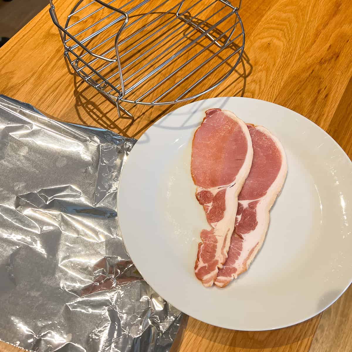 Bacon on a plate with some foil and an air fryer rack.