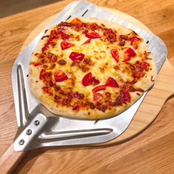 Sourdough pizza coming out of the oven on a pizza peel.