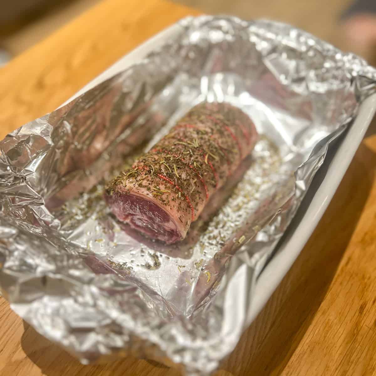 Roast lamb half way through cooking in a roasting tray.