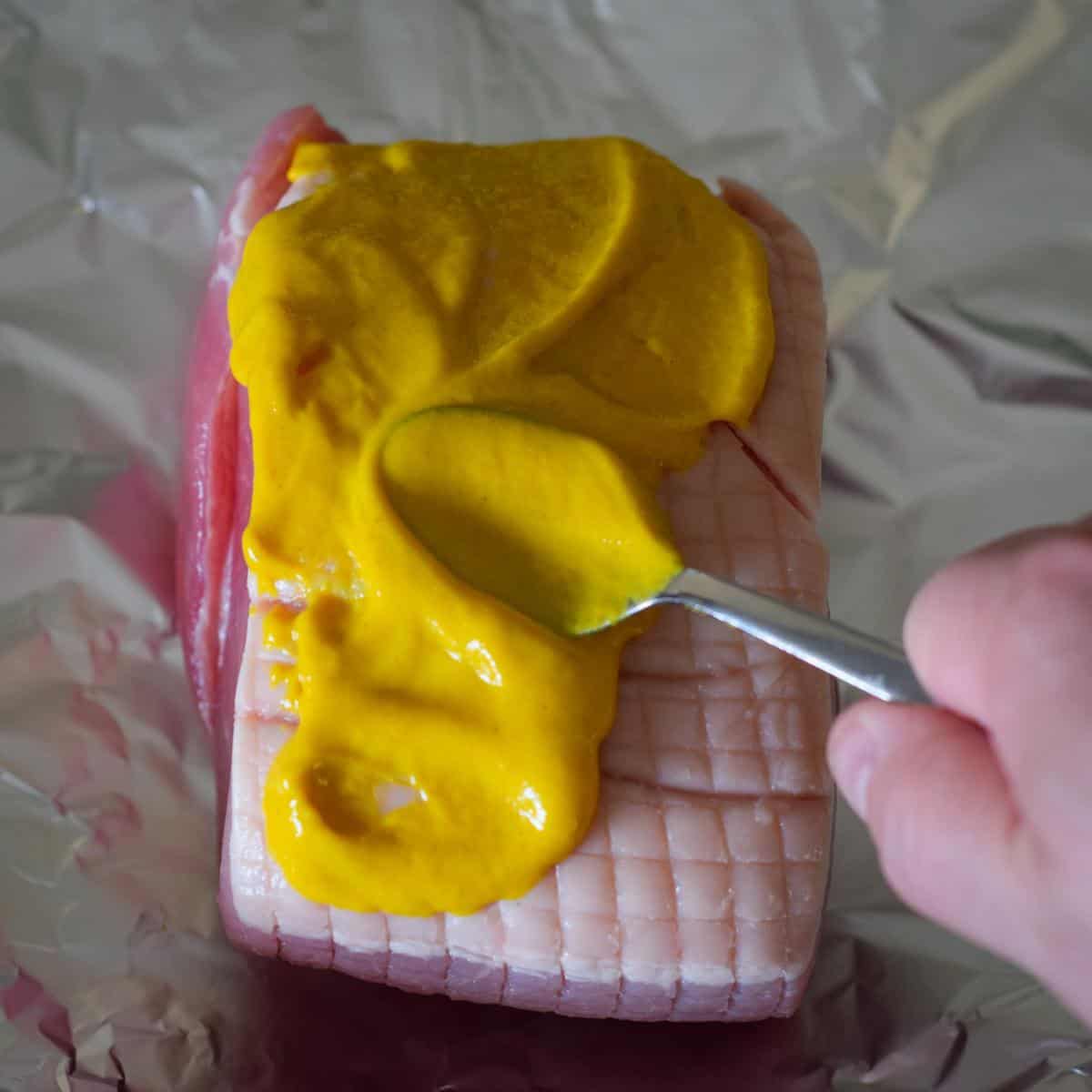 Coating a gammon in mustard using a spoon.