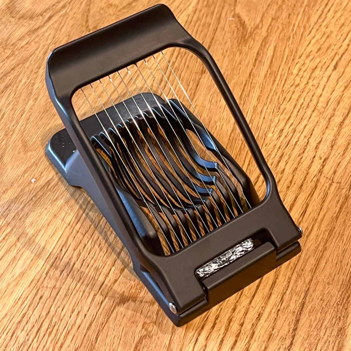 Black kitchen egg slicer with adjustable blades on wooden surface.