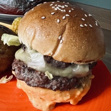Tasty beef burger with sesame seed bun on orange plate.